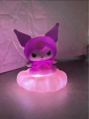 Kuromi lila nattlampa på rosa moln - Söt nattlampa i form av Kuromi från Sanrio, sittandes på ett rosa moln. Lampan lyser i lila och rosa toner och är gjord av plast. Perfekt som dekoration eller mysbelysning i rummet för dig som gillar kawaii och anime. Mått ca 8x10cm