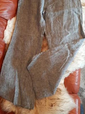 Grå linnebyxor med rak passform för vårkläder  - Säljer ett par grå linnebyxor med rak passform. Byxorna har en enkel design utan synliga detaljer och är perfekta för en avslappnad och stilren look. Tillverkade i linne för en luftig känsla. Storlek UK 16/EU 46. Mått på bilderna.