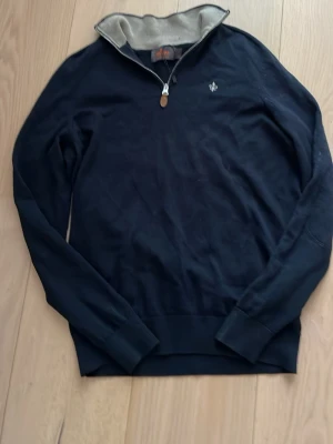 Mörkblå tröja med halv dragkedja - Stilren mörkblå tröja från Morris med halv dragkedja och liten logga på bröstet. Tröjan har ribbade muddar och en kontrastfärgad insida på kragen. Perfekt för en avslappnad men snygg look.