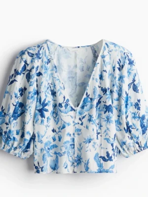 Blommig blåvit blus med puffärm - Fräsch blus i vitt med blått blommönster och djup V-ringning. Puffiga korta ärmar och knappar framtill. Aldrig använd