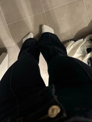 Mörkblå bootcut jeans med kontrastsömmar - Säljer ett par mörkblå bootcut jeans med tydliga vita kontrastsömmar och hög midja. Jeansen har klassisk femficksdesign och stängs med knapp och dragkedja. Materialet är stretchigt denim som sitter snyggt och bekvämt.