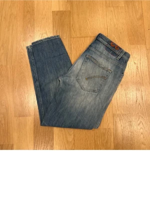 Blå slitna jeans med tvättade detaljer - Säljer ett par blå jeans med tvättade och slitna detaljer, klassisk femficksmodell och normal midja. Jeansen har en snygg vintage-look med slitningar på framsidan och ljusare partier. Perfekta för en avslappnad och trendig stil.