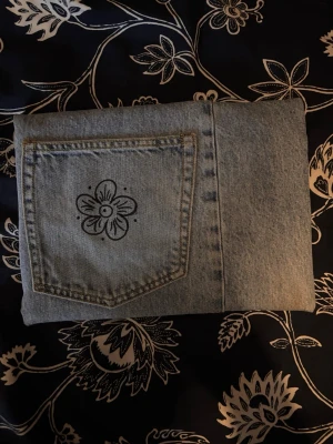 Ljusblått jeansfodral med blomma på fickan - Säljer ett ljusblått jeansfodral med en cool handritad blomma på bakfickan. Jeansen har klassisk femficksdesign och är gjorda i denim. Perfekt för dig som vill ha något unikt och utstickande i vardagen. Materialet inuti är även vattentätt. Passar mindre datorer som 13 och 14 tum. De är även handgjorda så inte perfekta. Men ett perfekt val för en bättre miljö!🌏(Materialet är köpt second hand)
