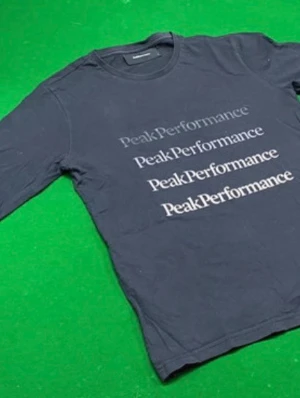 Svart långärmad Peak Performance tröja - Snygg svart långärmad tröja från Peak Performance med tryck i vitt framtill. Tröjan har rund hals och är tillverkad i mjukt bomullsmaterial. Perfekt för en sportig och avslappnad stil.