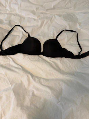 Svart plunge push up bh - En enkel och stilren svart push-up bh med släta kupor och justerbara axelband. Bh:n har bygel och stängs med hakar i ryggen. Liten i kupan. Helt ny då jag beställde fel storlek