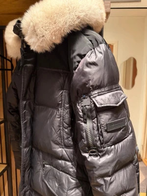 Rockandblue Dunjacka  - Säljer en superfin och varm Rockandblue-jacka i storlek L. Använd max 3 gånger, så den är i väldigt fint skick. Köpt från Thernlunds i Stockholm för 4999kr.  Varm & bekväm Klassisk svart – passar allt Avtagbar huva med pälsdetalj (fuskpäls)  Finns ett mycket litet hål längst ner vid ärmslutet, inget som syns eller stör helhetsintrycket (knappt märkbart, se bild.   Det är bara att skriva om du har några funderingar eller vill ha fler bilder på jackan. 