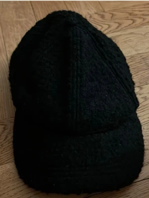 Svart stickad keps - Snygg svart keps med stickad struktur och klassisk böjd skärm. Perfekt accessoar för en cool och avslappnad stil. Kepsen har en unik textur som sticker ut och passar till många outfits.