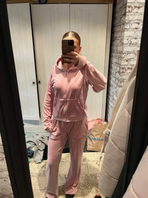Rosa mjukis sett - Mysigt rosa loungewear-set i velour med zip-hoodie och matchande byxor. Hoodien har dragkedja, fickor och ribbade muddar. Byxorna är raka och har resår i midjan för extra komfort. Äkta juicy. Aldrig använt