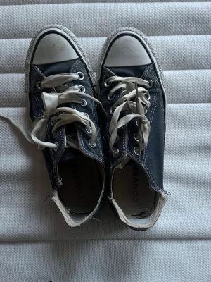 Svarta Converse låga sneakers - Klassiska svarta Converse sneakers med vit tå och sula. Skorna har vita satin snören och tydliga sömmar längs kanterna. Tillverkade i canvas med gummisula och låg profil som ger en avslappnad streetstil.