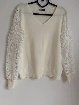 Vit stickad tröja med spetsärmar SHEIN - Trendig vit stickad tröja från SHEIN med v-ringning och unika spetsärmar i blommigt mönster. Tröjan har ribbade muddar och en avslappnad passform. Perfekt för dig som vill ha något extra till din outfit.