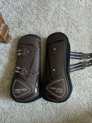 Bruna benskydd Lami-Cell Pro häst - Säljer ett par bruna benskydd från Lami-Cell Pro. Ordinarie pris 750kr. Använda 2 gånger dock lite slitage pågrund av att hästen som hade dom slog i mycket. De har dubbla elastiska remmar och är tillverkade i slitstark plast med mjuk insida. Märket och modellen står tydligt på skydden. Snygg design och praktiska detaljer. Skriv gärna om du undrar något! Pris kan också diskuteras