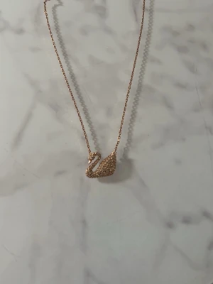 Guldfärgat halsband med svanberlock - Ett elegant halsband i guldfärg med en svanformad berlock. Framsidan av svanen är fylld med diamanter❤️ Original pris är 1500 därav priset. Skriv för mer frågor! Matchande med svanörhängena på min profil . Märket är de klassiska Swarovski❤️
