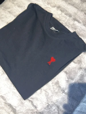 Svart t-shirt från Ami Paris - Säljer en svart t-shirt från Ami Paris med det ikoniska röda hjärtlogotypen broderad på bröstet. Klassisk rund hals och korta ärmar. Tillverkad i mjuk bomull för en skön känsla och enkel stil.