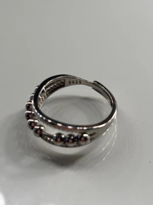 Snygg silverring med pärldetaljer - Cool ring i äkta silver (925) med en unik design där en rad silverpärlor löper längs ovansidan(stressring). Ringen har en öppen justerbar form och glänsande finish som ger en modern vibe. Perfekt för dig som gillar stilrena accessoarer med det lilla extra.