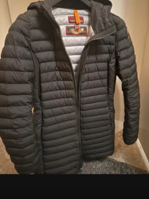 Svart dunjacka från Parajumpers - Snygg svart dunjacka från Parajumpers med quiltad design och huva. Jackan har dragkedja framtill, diskret logga på ärmen och lätt vaddering som håller dig varm under kalla dagar. Insidan är ljusgrå och materialet är lätt men isolerande.