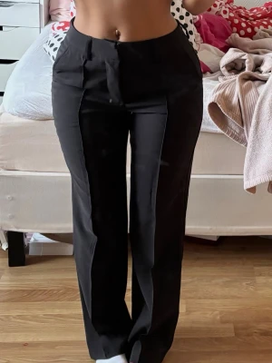 Svarta raka kostymbyxor - Säljer ett par svarta kostymbyxor med hög midja och raka ben. Byxorna har pressveck framtill och stängs med dragkedja och hake. Klassisk och stilren modell som passar till många olika looks.