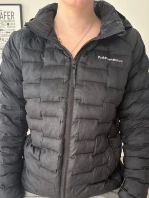 Svart dunjacka Peak Performance - Snygg svart dunjacka från Peak Performance med huva och dragkedja framtill. Jackan har quiltad design. Nypris ca 1500. Använd varsamt förutom att den har ett litet hål på baksidan som vi har satt en lapp på (se bild 3)☺️☺️