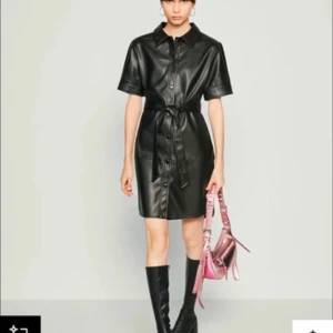 Skjortklänning / klänning i skinnimitation i XS. Noisy May - Svart kortärmad midiklänning i skinnimitation  med knappar framtill & matchande bälte i midjan. En aning oversize. Använd en enda gång. Längdmått: mätt från baksidan: ca 90 cm.