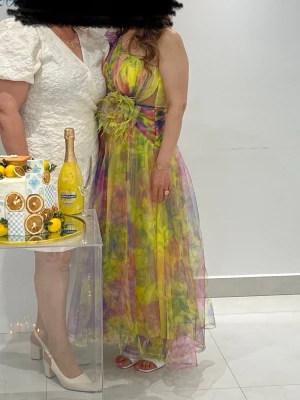 Färgglad långklänning med mönster - Säljer en maxiklänning i flera färger med blommigt mönster och markerad midja. Klänningen har en stor dekorativ blomma i midjan och tunna axelband. Materialet är lätt och skirt, perfekt för sommarens alla tillfällen. Köpt i London. Pris kan diskuteras. 