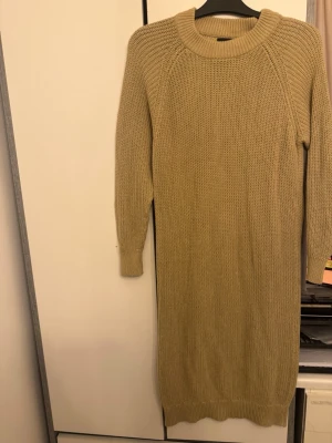 Beige stickad klänning från Pieces - Stickad klänning i beige från Pieces med rund halsringning och långa ärmar. Grovstickad struktur och ribbade muddar vid hals, ärmslut och nederkant. Perfekt för lager på lager och enkel att styla med boots eller sneakers.