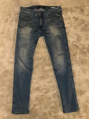 Replay Anbass - Säljer ett par blå slim fit jeans från Replay med snygga slitningar och klassiska fem fickor. Jeansen har en något tvättad look och smala ben. Perfekta för dig som gillar en modern och avslappnad stil.