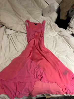 Rosa långklänning med volang - Säljer en rosa långklänning i tunn, flowy chiffong med volangdetaljer nertill. Klänningen har breda axelband och en lös, svepande passform som ger en romantisk vibe. Perfekt för dig som gillar färg och vill sticka ut.