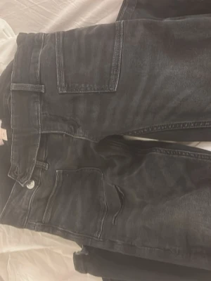 Svarta jeans från Gina Tricot - Säljer ett par svarta jeans från Gina Tricot med raka ben och flera praktiska fickor på sidorna. Byxorna har knapp- och dragkedjestängning samt breda hällor för bälte. Materialet är slitstarkt och passar perfekt till en streetwear-look.