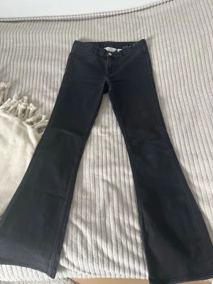 Svarta bootcut jeans med låg midja - Snygga svarta bootcut jeans med låg midja och klassisk femficksdesign. Jeansen har vida ben och är tillverkade i ett stretchigt denimtyg som sitter bekvämt. Perfekta för dig som vill ha en trendig siluett och gillar retrovibbar.