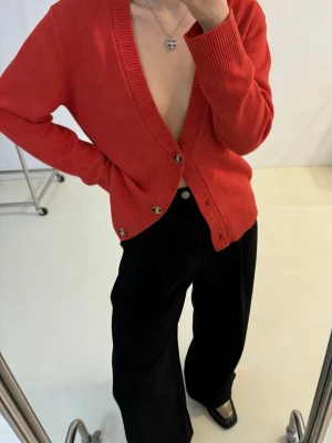 Marimekko Röd kofta i ullmix med knappar - Snygg röd kofta med djup V-ringning och stora knappar framtill. Tillverkad i en mjuk ull- och bomullsblandning som känns skön mot huden. Ribbstickade muddar vid ärmslut och nederkant ger en clean look. Perfekt att styla lager på lager.