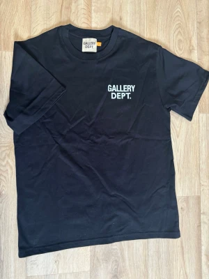 Black t-shirt from Gallery Dept. - Säljer en svart t-shirt från Gallery Dept. med tryckt logga på bröstet. Klassisk rund hals och korta ärmar. Tillverkad i mjuk bomull för skön känsla och enkel stil. Perfekt till jeans eller shorts för en clean look.