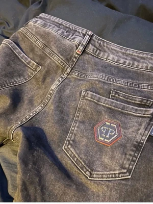 Svarta jeans från Philipp Plein - Säljer ett par svarta jeans från Philipp Plein med klassisk femficksmodell och ett snyggt PP-märke på bakfickan. Jeansen har en tvättad look och raka ben. Perfekta för dig som gillar streetwear och vill ha något som sticker ut. Säljer byxorna eftersom jag har tröttnat på det klädstilen.