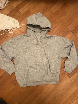 Grå basic hoodie med huva - En enkel och stilren grå hoodie med huva och dragsnören. Hoodien har en avslappnad passform, ribbade muddar vid ärmar och nederkant samt är tillverkad i mjukt sweatshirtmaterial. Perfekt för en chill och casual look.
