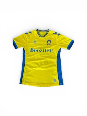 Gul Brøndby IF matchtröja Hummel - Snygg gul Brøndby IF matchtröja från Hummel med blå detaljer och tryck. Tröjan har klubbmärke och sponsorlogga på bröstet samt spelarnamn och nummer 5 på ryggen. Tillverkad i lätt och ventilerande material, perfekt för fotbollsträning eller match eller ett nyförvärv till samlingen.