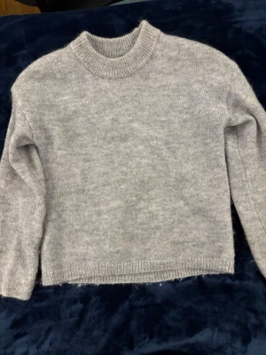 Ull&mohair mix stickad tröja Kappahl - Mysig ljusgrå stickad tröja från Kappahl i storlek XS. Tröjan har rund halsringning, långa ärmar och ribbade muddar vid hals, ärmslut och nederkant. Perfekt för kalla dagar och enkel att matcha med olika outfits.