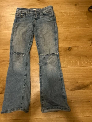 Ljusblå bootcut jeans med slitningar - Ljusblå jeans i bootcut-modell med slitna detaljer och hål vid knäna. Klassisk femficksdesign och låg midja. Jeansen har en avslappnad passform och är tillverkade i denim. Perfekta för en cool och avslappnad stil. Köpa för ca 400/350kr