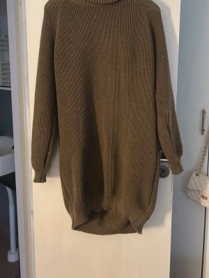  stickad klänning i beige - En  stickad klänning i beige med hög krage och långa ärmar. Tröjan har ribbstickade muddar och en längre passform baktill. Perfekt för lager-på-lager och chill stil.