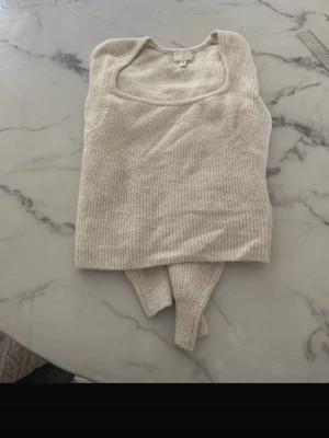 Beige stickad långärmad  - Trendig beige ribbad linnetopp med fyrkantig ringning. Toppen är ärmlös och har en croppad passform som passar perfekt till höga jeans eller kjol. Mjuk och stretchig kvalitet för en bekväm känsla.