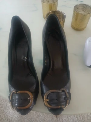 Svarta pumps med stor spänne - Snygga svarta pumps med rundad tå och stor dekorativ metallspänne framtill. Klacken är i trälook och har en klassisk form som ger extra höjd. Skorna är tillverkade i läder och har en tidlös design som passar till många olika outfits. Pris kan diskuteras!🥰