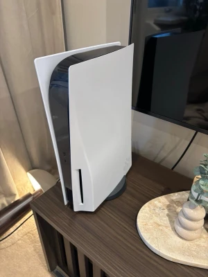 PlayStation 5  - Säljer en PlayStation 5 konsol från Sony. Konsolen har en futuristisk design i vitt och svart med rundade kanter och står på en rund svart fot. Materialet är plast och den har inbyggd skivläsare för ● fysiska spel. Perfekt för gaming och streaming! Ingen box Elr kvitto, 1 kontroll medföljer 