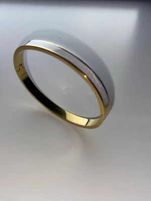 Guldigt armband i metall  - Snyggt stelt armband i guldfärgad metall med enkel och stilren design. Armbandet är runt och har en slät yta utan dekorationer, vilket gör det lätt att matcha med andra smycken. Perfekt accessoar för dig som gillar minimalistisk stil. Den är ganska liten runt handleden så perfekt för dig med mindre handleder. 