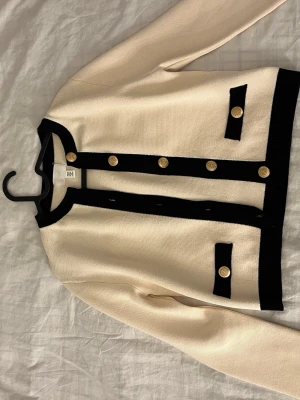 Vit fin kofta med guld knappar  - En Vit svart fin kofta med guldiga knappar. Köpt på H&M och använt endast 1 gång innan. Jätte fin kofta som funkar både för fin klädda sammanhang men har själv använt den till vardagen. Säljer endast pågrund av att den inte kommer till användning.