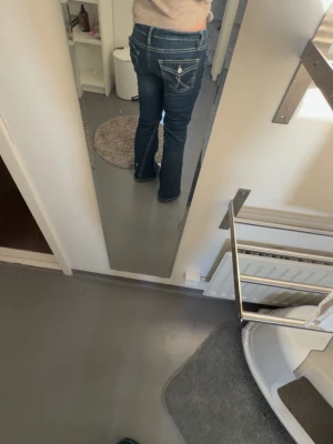 Blå bootcut jeans med vita sömmar - Säljer ett par blå bootcut jeans med vita kontrastsömmar och dekorativa fickor bak. Jeansen har normal midja och klassisk femficksdesign. Perfekta för en avslappnad och trendig look. Strl 164 från Gina 