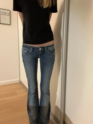 Blå bootcut jeans med broderade fickor - Säljer ett par blå bootcut jeans med snygga slitningar och broderade bakfickor med knappdetaljer. Jeansen har låg midja och klassisk femficksdesign. De är i strl XS tall men skulle inte säga att de är jättelånga, för referens är jag 175 och de är lite för korta för mig. Är du runt 170 kommer de passa perfekt. Perfekta för dig som gillar en avslappnad men ändå trendig stil.