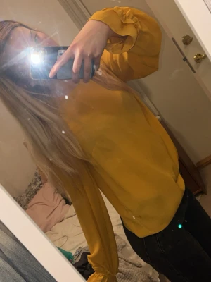 Gul blus med ballongärmar - Trendig gul blus med långa ballongärmar och rund halsringning. Tillverkad i ett lätt, flowy material som ger en snygg siluett. Perfekt att styla med jeans eller kjol för en cool look.