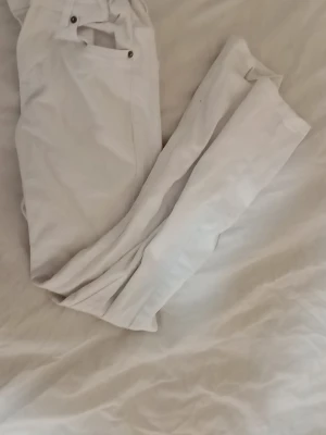 Vita raka jeans från Lindex  - Säljer ett par vita jeans från Detroit med raka ben och klassisk femficksmodell. Jeansen har metallknappar och detaljer samt en snygg patch med märkesnamnet bak i midjan. Perfekta för en clean och stilren look.