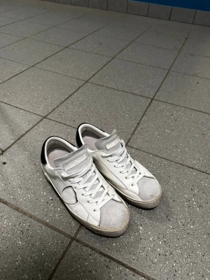 Philippe Model - Säljer ett par vita låga sneakers från Philippe Model med svart hälflik och grå detaljer på tån. Skorna har klassisk snörning, perforerade sidor och är tillverkade i läder med mockadetaljer. Perfekta för en clean och stilren look. Priset är ej hugget i sten så varm inte rädda att ställa frågor 😁