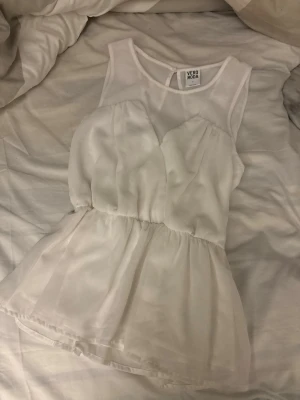 Vit ärmlös blus från Vero Moda - Säljer en söt vit blus från Vero Moda. Toppen är ärmlös med transparent mesh upptill och omlottdetalj i ryggen. Den har en lätt utsvängd passform och markerad midja, perfekt till jeans eller kjol.
