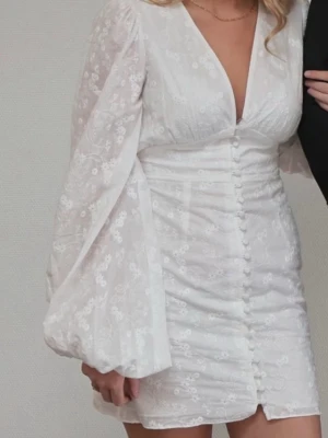  klänning från Adoore  - Superfin vit klänning från Adoore med blommigt mönster, v-ringning och långa puffärmar. Klänningen har knappar framtill och är sydd i ett lätt, luftigt material som passar perfekt till sommaren. Aldrig använd!!!