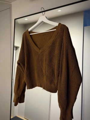 Brun croppad stickad tröja - Säljer en brun croppad stickad tröja med djup v-ringning och långa, vida ärmar.