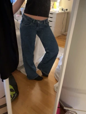Blåa raka jeans med låg midja från Gina - Säljer ett par nästan helt nya blåa raka jeans med låg midja och klassisk femficksdesign. Jeansen har en avslappnad passform och är perfekta för en trendig och bekväm look. Materialet är denim i bomull och färgen är mellanblå. 